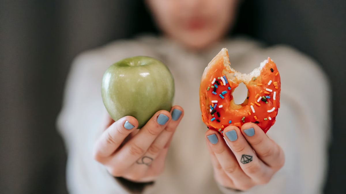 Crop anonymous female demonstrating delicious sweet donut and fresh green apple while making decision