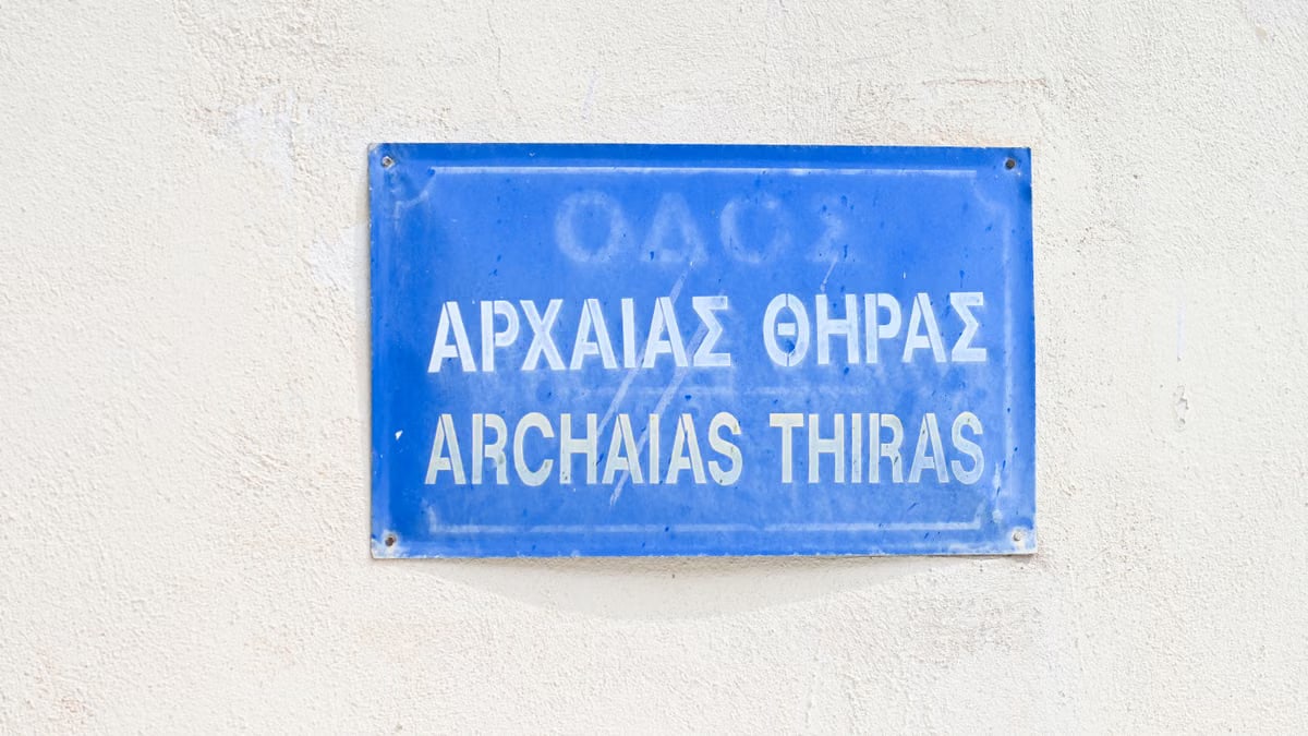 A vibrant blue street sign with Greek and English text, symbolizing Ancient Thira in Fira, Greece.